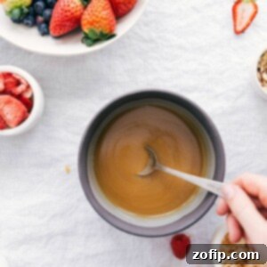 A close-up of the finished creamy vanilla sauce in a white ramekin, garnished with fresh berries and a mint leaf, highlighting its rich texture.
