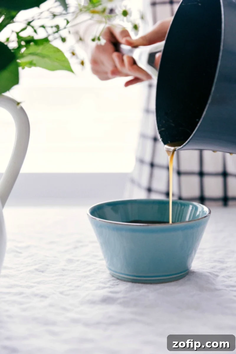 Close-up shot of rich, golden vanilla sauce being poured from a small pitcher into a serving bowl, showcasing its smooth, flowing consistency, ready to be enjoyed.