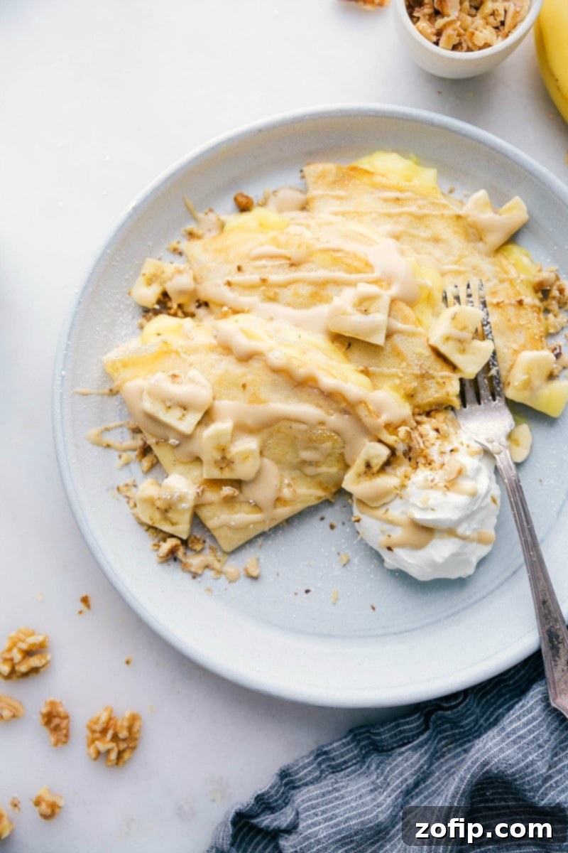A beautifully presented plate of Banana Crepes, featuring banana slices artfully cut into heart shapes. The crepes are golden brown and lightly dusted, suggesting a sweet and inviting flavor. This overhead shot highlights the delicious filling and elegant presentation.