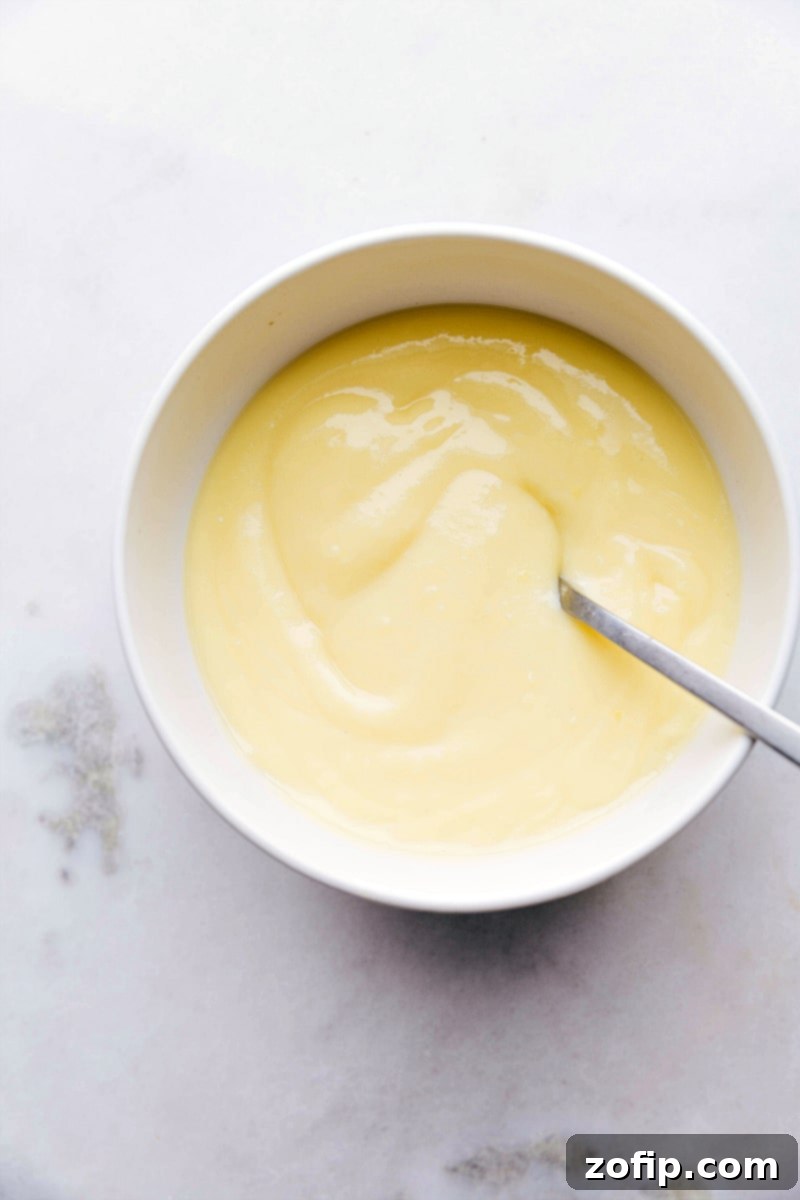 Close-up of a bowl filled with smooth, creamy custard filling for banana crepes. The custard has a rich, golden hue, indicating its luscious texture and appealing flavor.