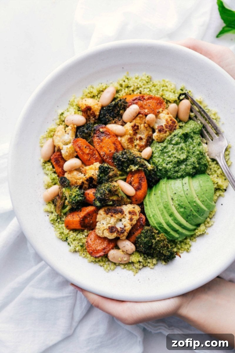 Delicious Pesto Roasted Vegetable Bowls with perfectly roasted cauliflower, broccoli, carrots, and white beans atop 5-minute pesto couscous. A flavorful, protein-rich, and healthy vegetarian recipe perfect for any meal. Overhead image of the ready-to-eat Pesto Roasted Veggie Bowls, showcasing vibrant roasted vegetables and pesto couscous, garnished with fresh avocado and almonds.