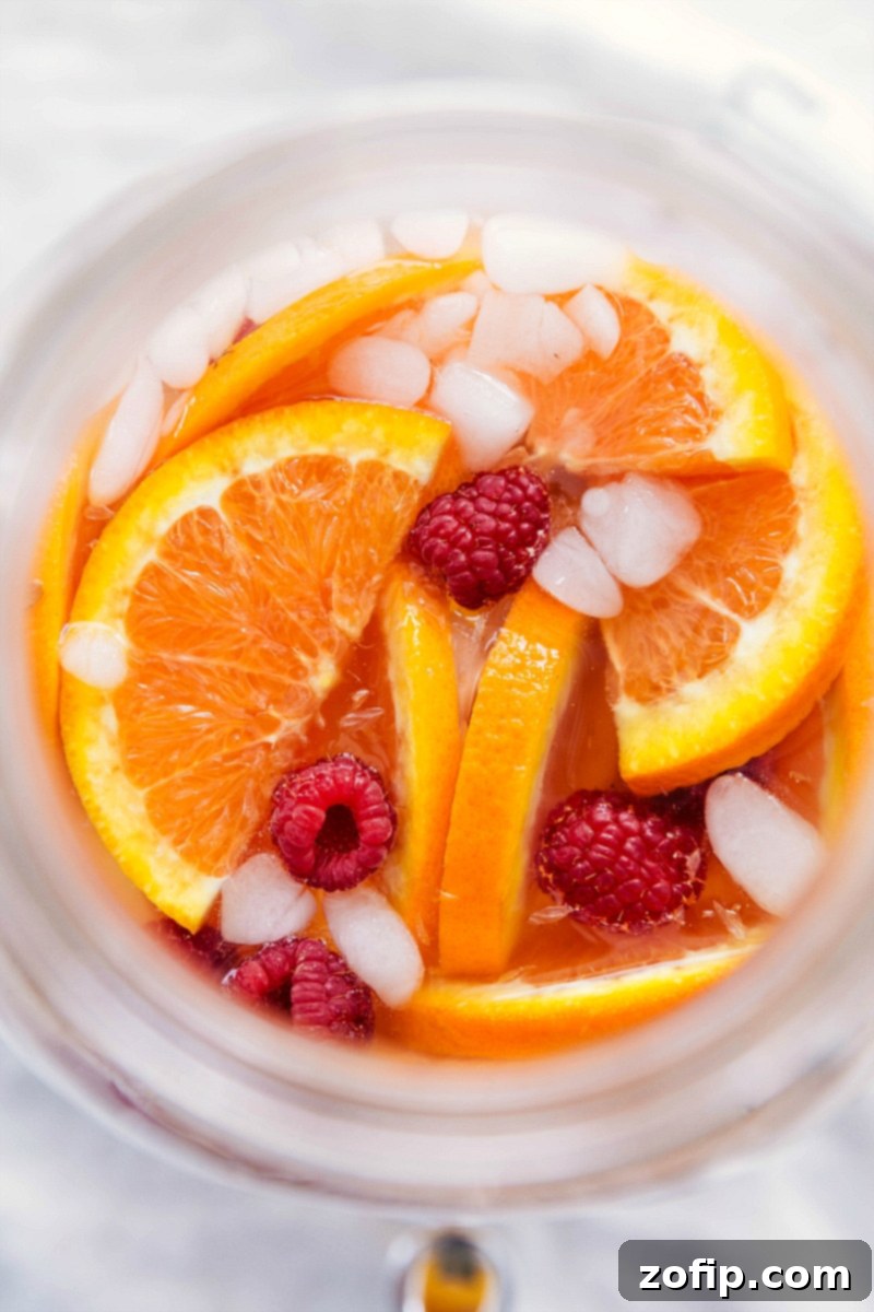 A vibrant glass of white grape punch garnished with fresh Cara Cara orange slices, raspberries, and ice, ready to be enjoyed as a refreshing and beautiful drink.