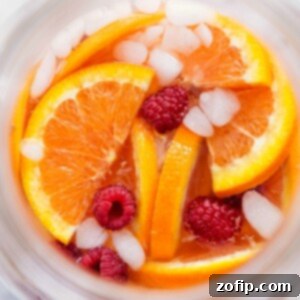 A glass of delicious white grape punch garnished with fresh Cara Cara orange slices and raspberries, with ice, ready to be served and enjoyed.