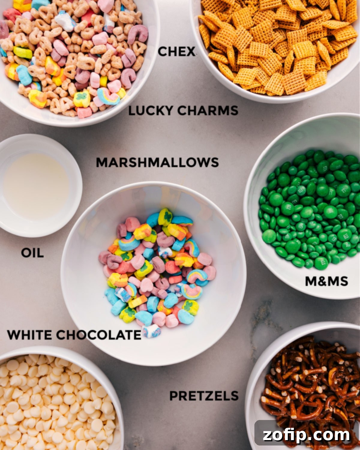 All the ingredients for this Leprechaun Bait recipe are prepped and ready for easy assembly, including Chex cereal, Lucky Charms, green M&Ms, mini marshmallows, vegetable oil, white chocolate chips, and mini pretzel twists.