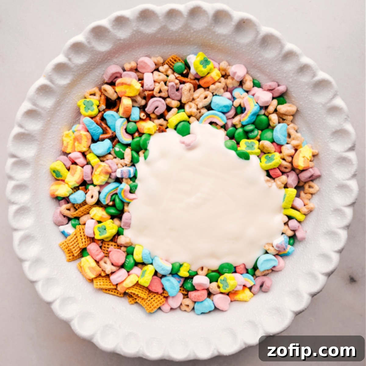 Melted white chocolate is being poured into the large bowl of Leprechaun Bait dry ingredients, ready to mix for a perfect St. Patrick's Day treat.