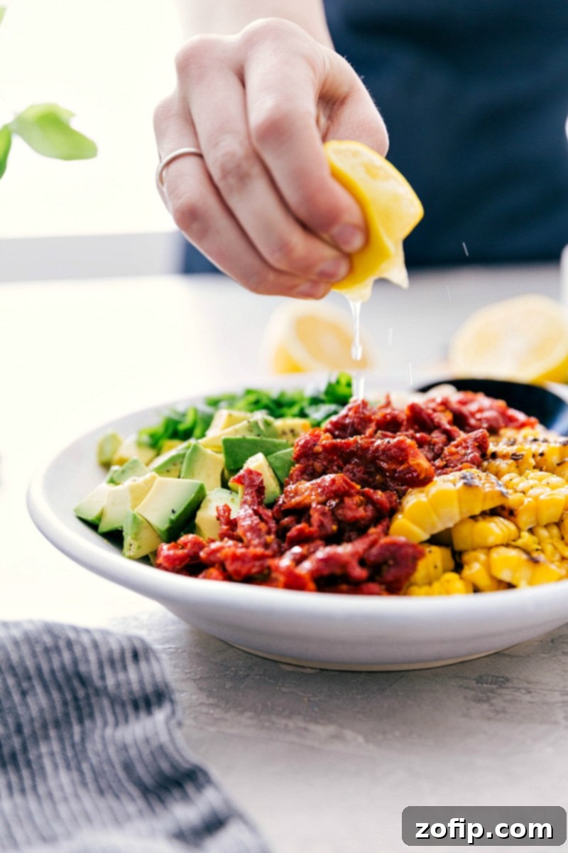 The best ever White Bean Salsa with creamy avocado, crisp corn, savory sun-dried tomatoes, fresh lemon, and sweet basil is our latest obsession! It's perfect over grilled Pesto Chicken, quinoa, or couscous (hello crave-able vegetarian meal!), or with some good tortilla chips. Recipe via Chelseasmessyapron #healthy #keto #whole #protein #whole30 #best #avocado #corn #sundriedtomatoes #clean #cleaneating #whitebean #salsa Close-up of lemon juice being drizzled over a fresh bowl of White Bean Salsa, highlighting the final touch