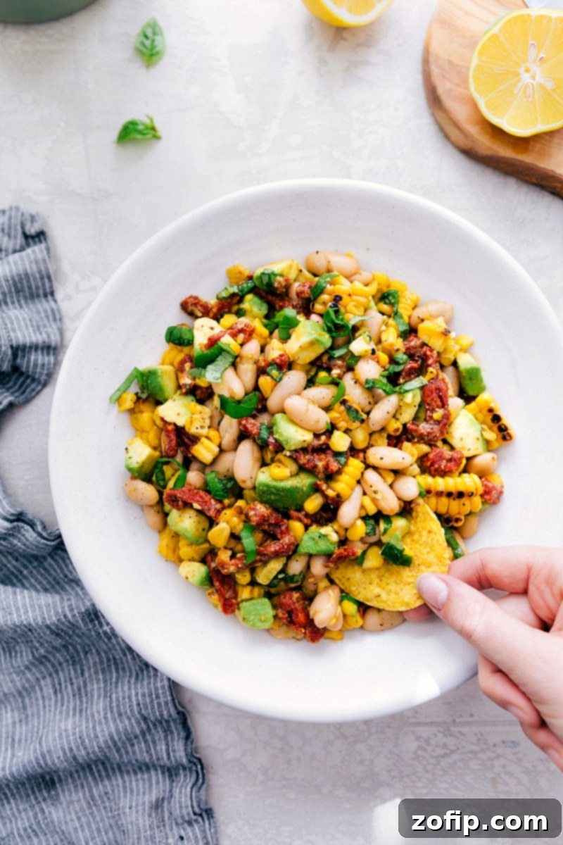 White Bean Salsa! Recipe via Chelseasmessyapron #healthy #keto #whole #protein #whole30 #best #avocado #corn #sundriedtomatoes #clean #cleaneating #whitebean #salsa Overhead shot of White Bean Salsa with a chip being dipped, ready to be enjoyed