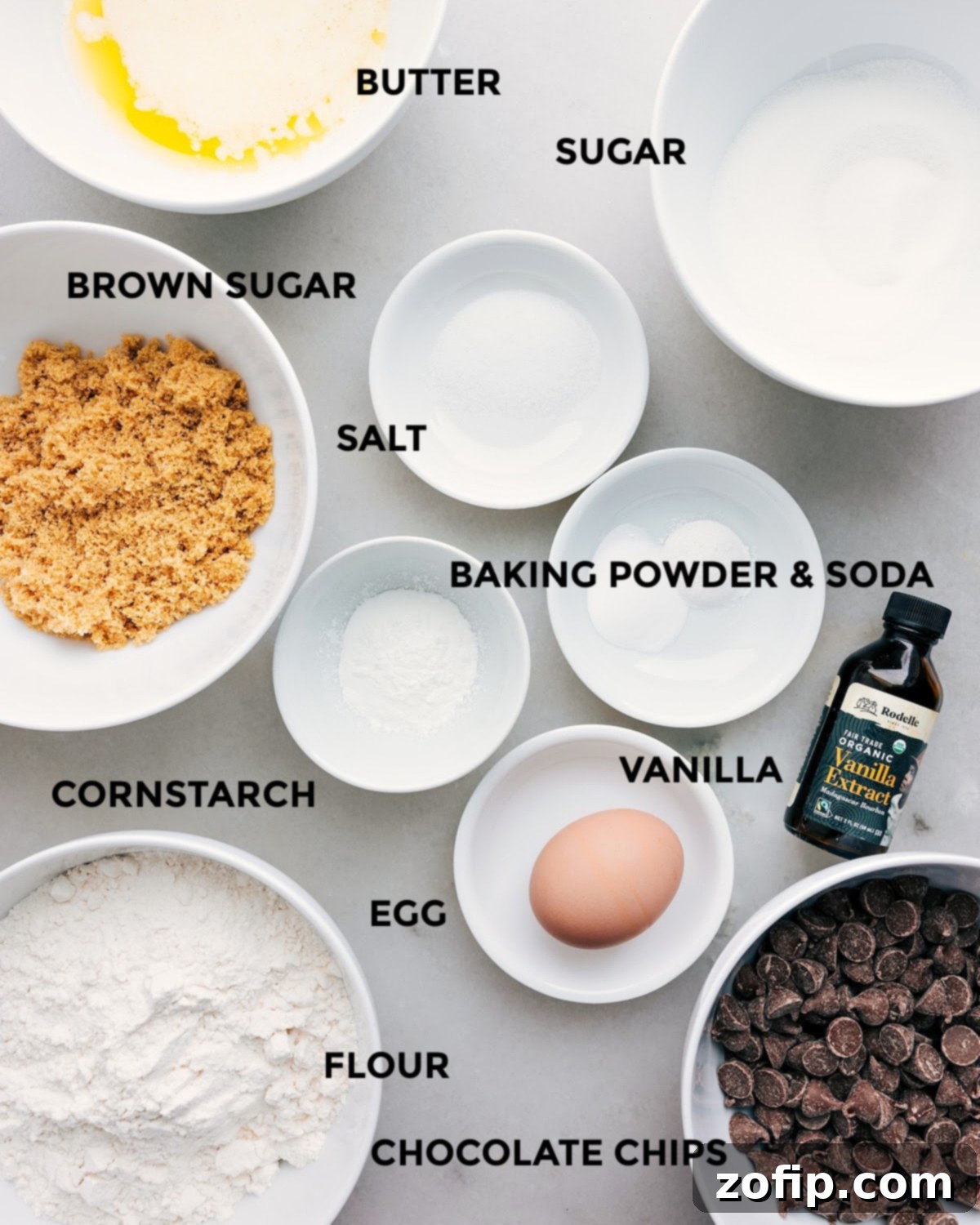 A flat lay photograph of all the ingredients prepped for easy assembly for bakery-style chocolate chip cookies, including butter, sugar, salt, baking soda, baking powder, vanilla, cornstarch, egg, flour, and various chocolate chips.
