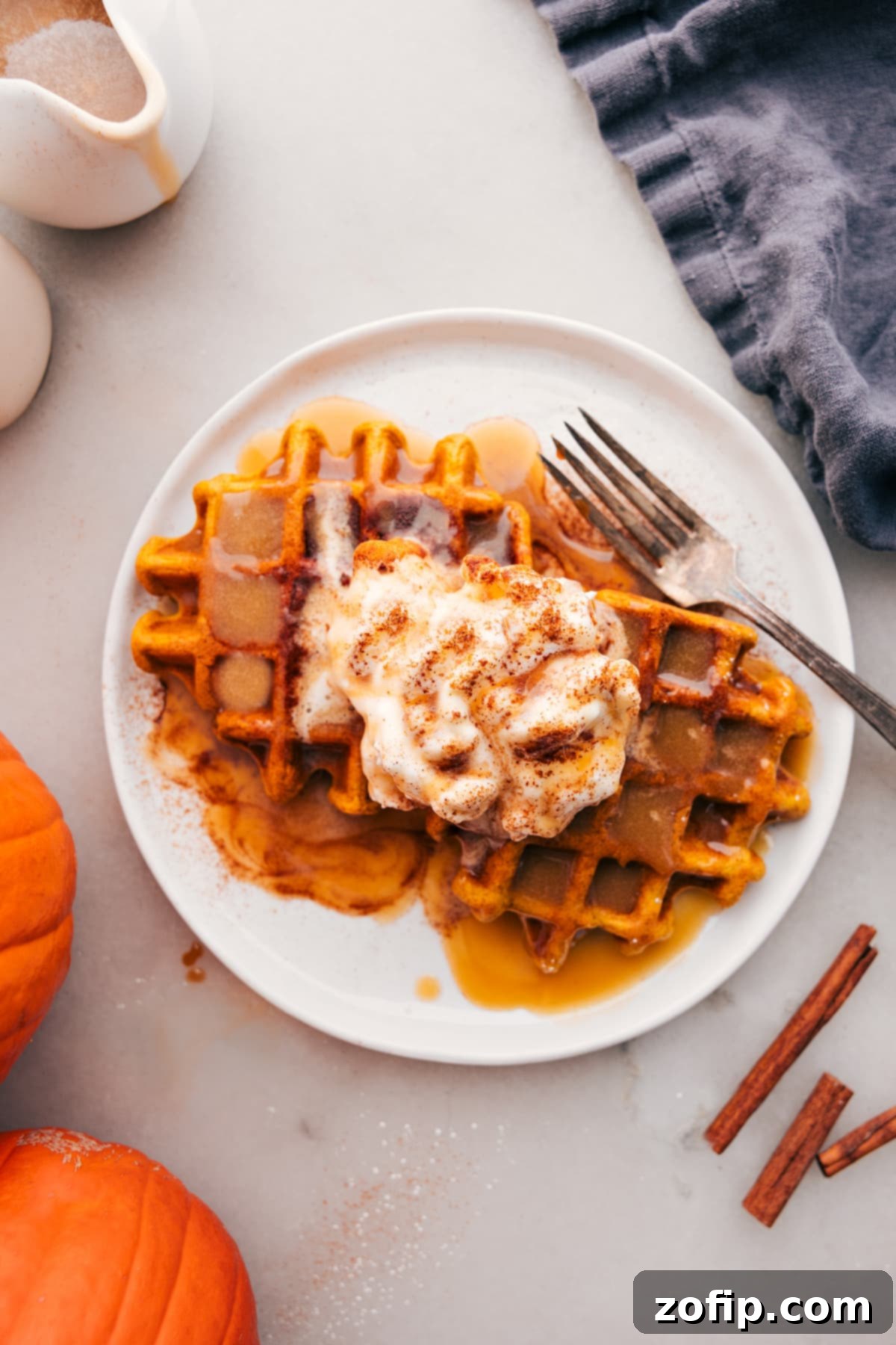 Golden pumpkin waffles stacked high, drizzled with maple syrup and topped with a generous dollop of fresh whipped cream, ready to be enjoyed.