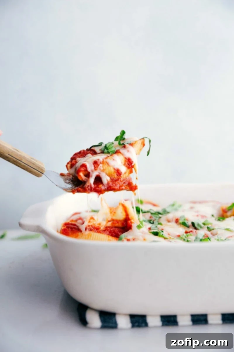 Spatula pulling up a golden-brown Stuffed Shells Recipe from the pan, showcasing the cheesy filling and rich marinara.