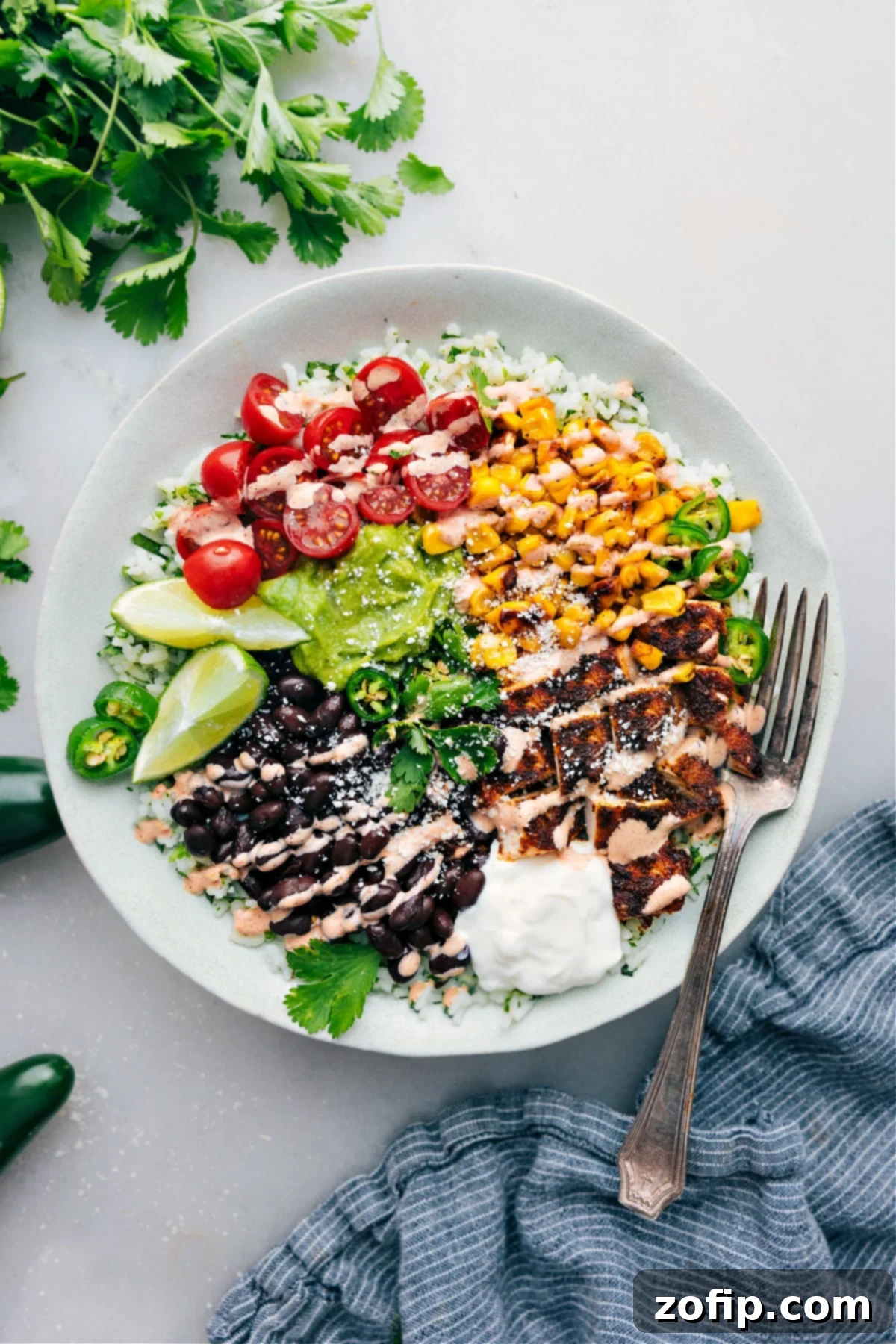 A vibrant chicken burrito bowl served with cilantro-lime rice, black beans, corn, fresh avocado, tomatoes, and a drizzle of creamy chili-lime sauce, ready to be enjoyed.