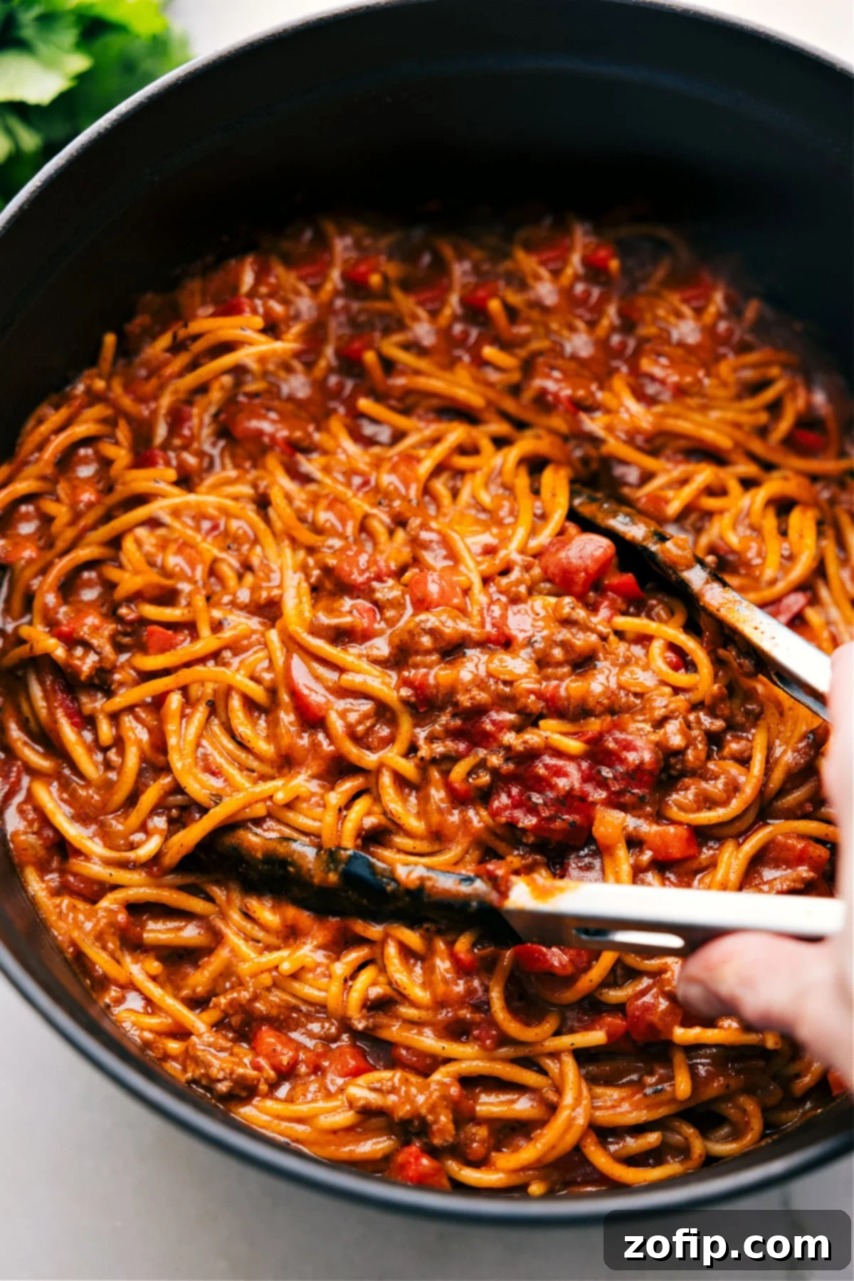 A large pot filled with the best One-Pot Taco Spaghetti, ready to be served, with tongs hovering above.