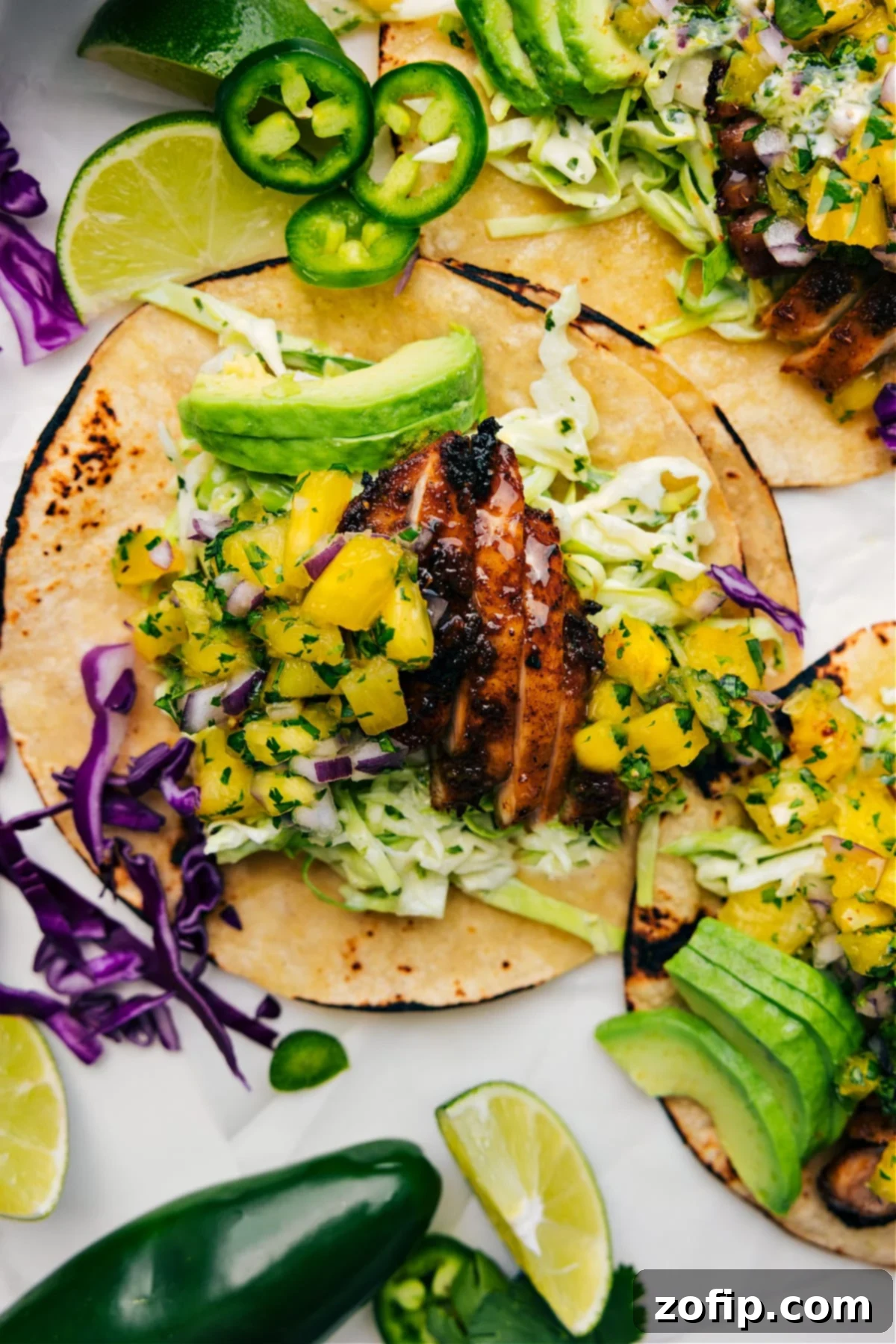 Close-up of three Jerk Chicken Tacos arranged neatly, showcasing vibrant mango salsa, creamy green sauce, and fresh cilantro garnish on a rustic background.