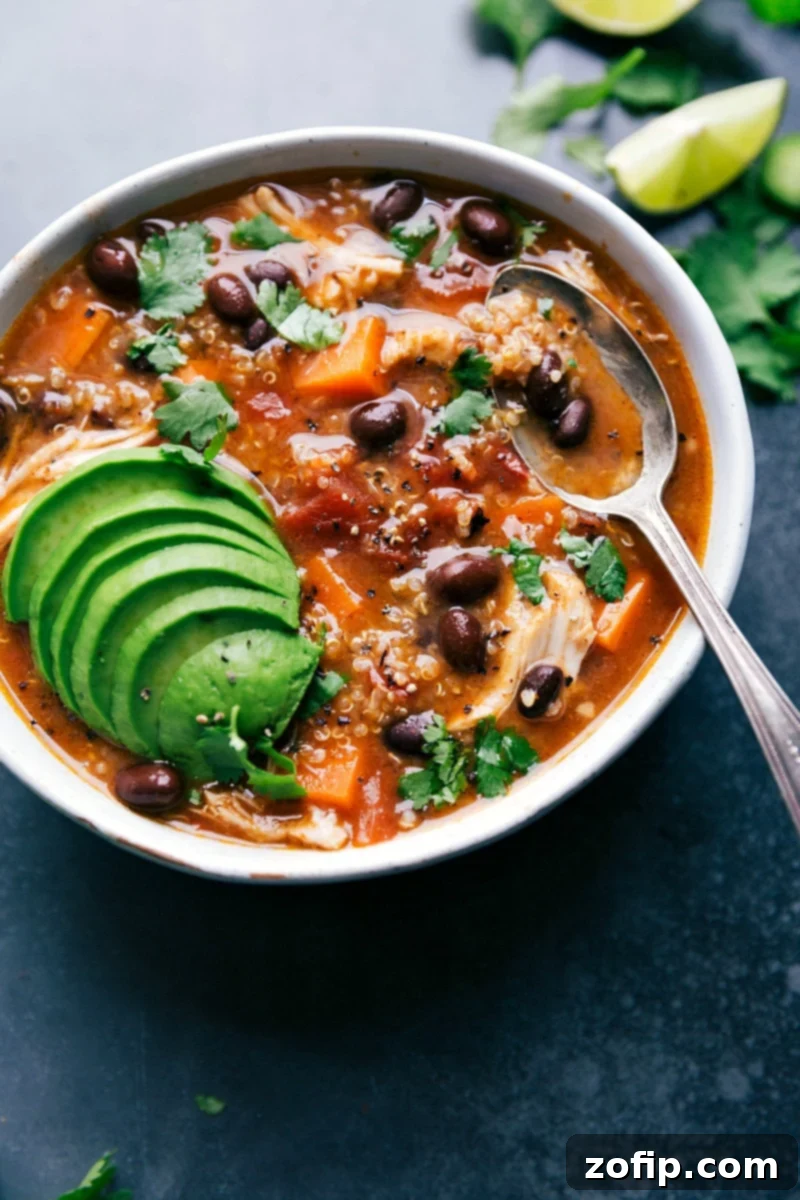 A generously sized bowl of warm sweet potato chicken soup, beautifully topped with fresh herbs and creamy avocado slices, ready for a wholesome meal.
