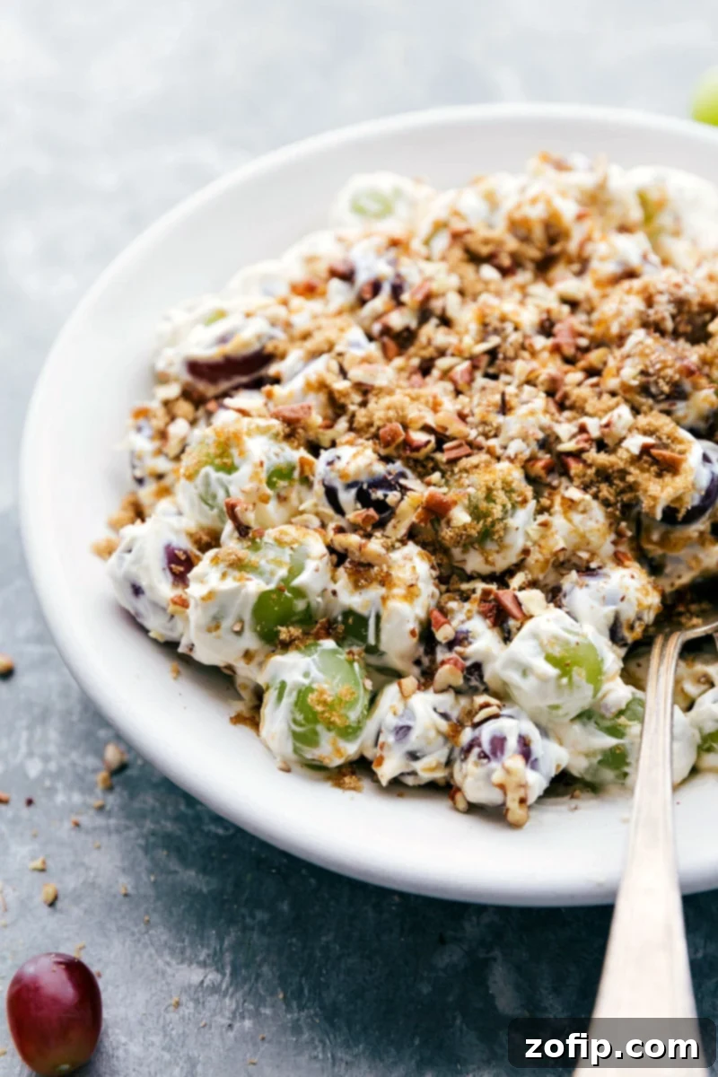A bowl of creamy Grape Salad with a serving spoon, adorned with a luscious topping of brown sugar and pecans, ready to be enjoyed.