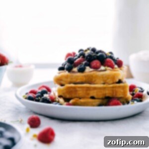 Stack of waffles with berries and whipped cream on top with syrup drizzling down.