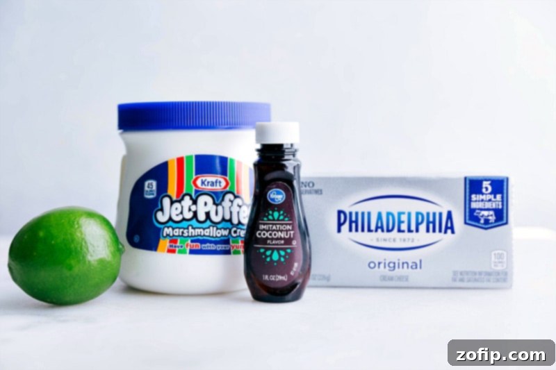 Image of all the key ingredients needed for the fruit dip: a block of cream cheese, a container of marshmallow fluff, a fresh lime, and a bottle of coconut extract, laid out on a clean surface.