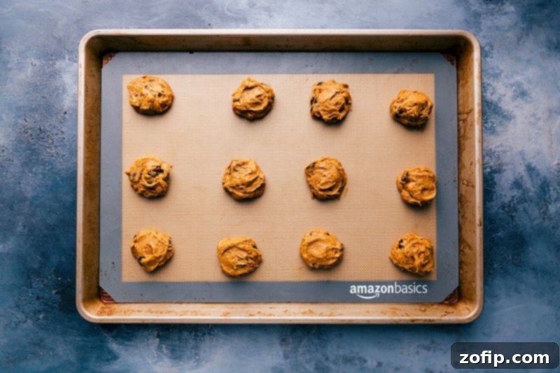 Rows of portioned pumpkin cookie dough, prepared with cake mix and chocolate chips, neatly arranged on a parchment-lined baking sheet, awaiting baking.