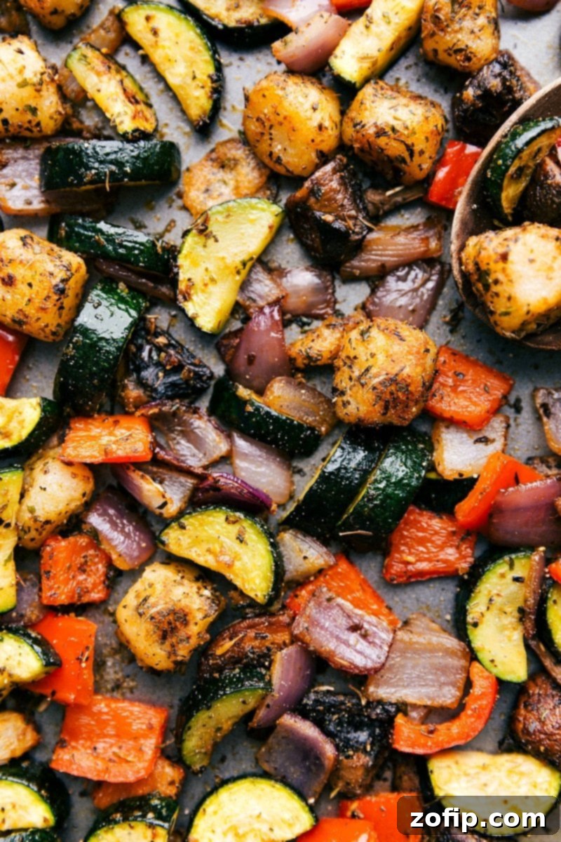Golden brown baked gnocchi mixed with colorful roasted vegetables, including zucchini, red bell pepper, and mushrooms, fresh out of the oven on a sheet pan, ready to be served.