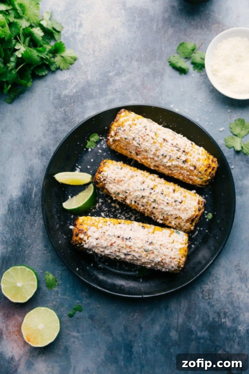 Ready-to-eat Mexican Street Corn (Elote) on a rustic plate, garnished with fresh lime wedges and chopped cilantro, showcasing its perfectly roasted kernels and creamy coating.