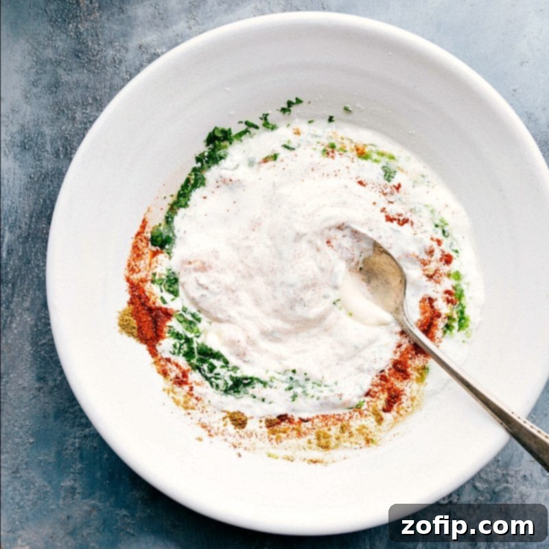 Creamy Elote sauce being mixed in a bowl with various spices, showcasing the rich texture and vibrant colors before being spread on corn.