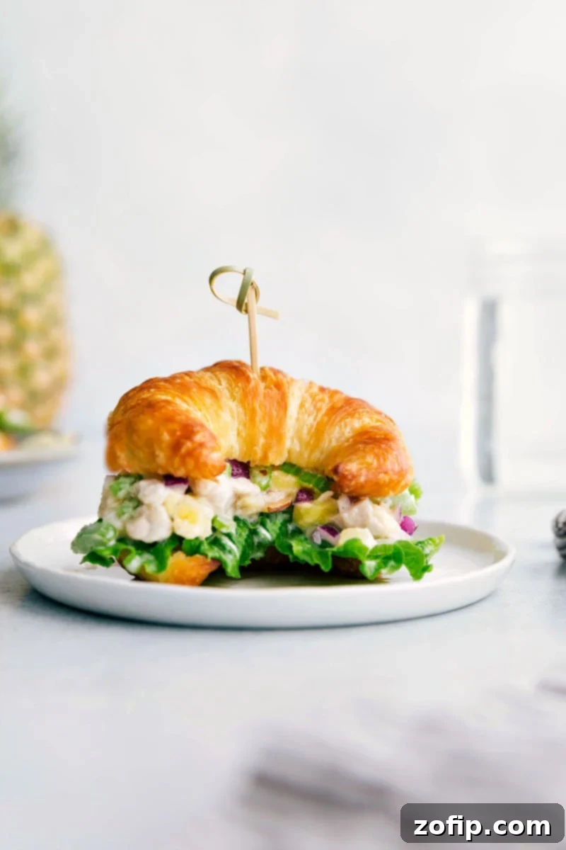 Pineapple chicken salad on a croissant, overflowing with flavorful ingredients, creating the perfect combination of savory and sweet. A delicious and refreshing summer meal.
