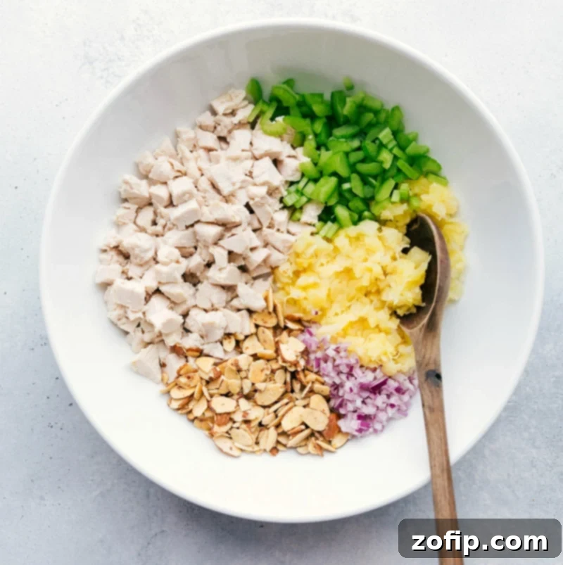 A bowl filled with cooked chicken, crushed pineapple, and other fresh ingredients, ready to be mixed together for a flavorful pineapple chicken salad.