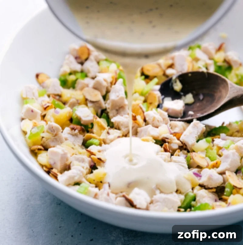 Creamy dressing being poured over the chicken salad with pineapple, ready to be mixed for a delicious meal, ensuring every bite is flavorful.