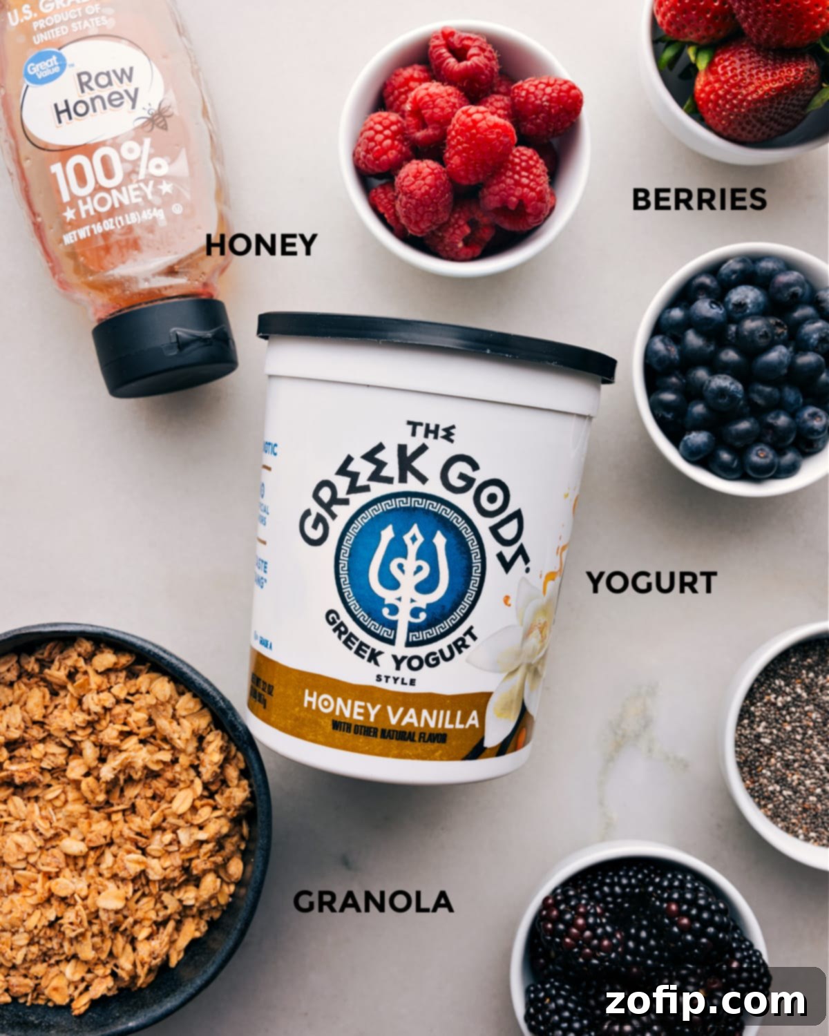 Prepped Ingredients for Yogurt Parfait All the fresh ingredients for a yogurt parfait laid out on a white surface: fresh mixed berries, a bowl of creamy yogurt, a jar of crunchy granola, and a honey dipper with golden honey, ready for assembly.