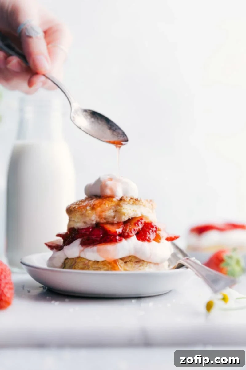 Moist and delicious strawberry shortcake with layers of fluffy cake, fresh strawberries, and whipped cream, strawberry sauce being drizzled on top.