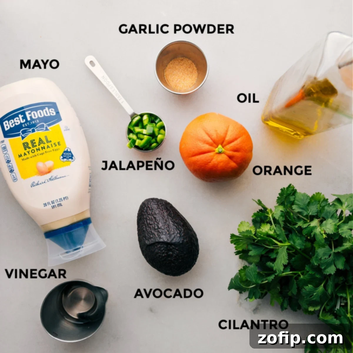 Ingredients for the Creamy Avocado Sauce in Chicken Rice Bowls Fresh ingredients for the creamy avocado sauce, including a ripe avocado, orange, white vinegar, jalapeño, cilantro, mayo, and honey, all prepped for blending.