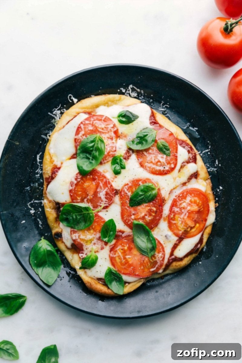 A delicious baked naan pizza on a plate, topped with fresh basil leaves, melted cheese, and vibrant toppings.