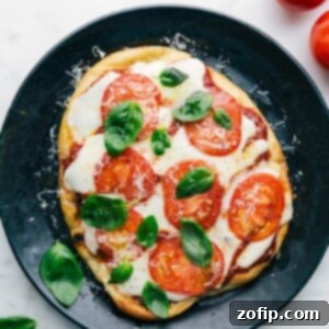 A delicious baked naan pizza on a plate, topped with fresh basil leaves, melted cheese, and vibrant toppings.