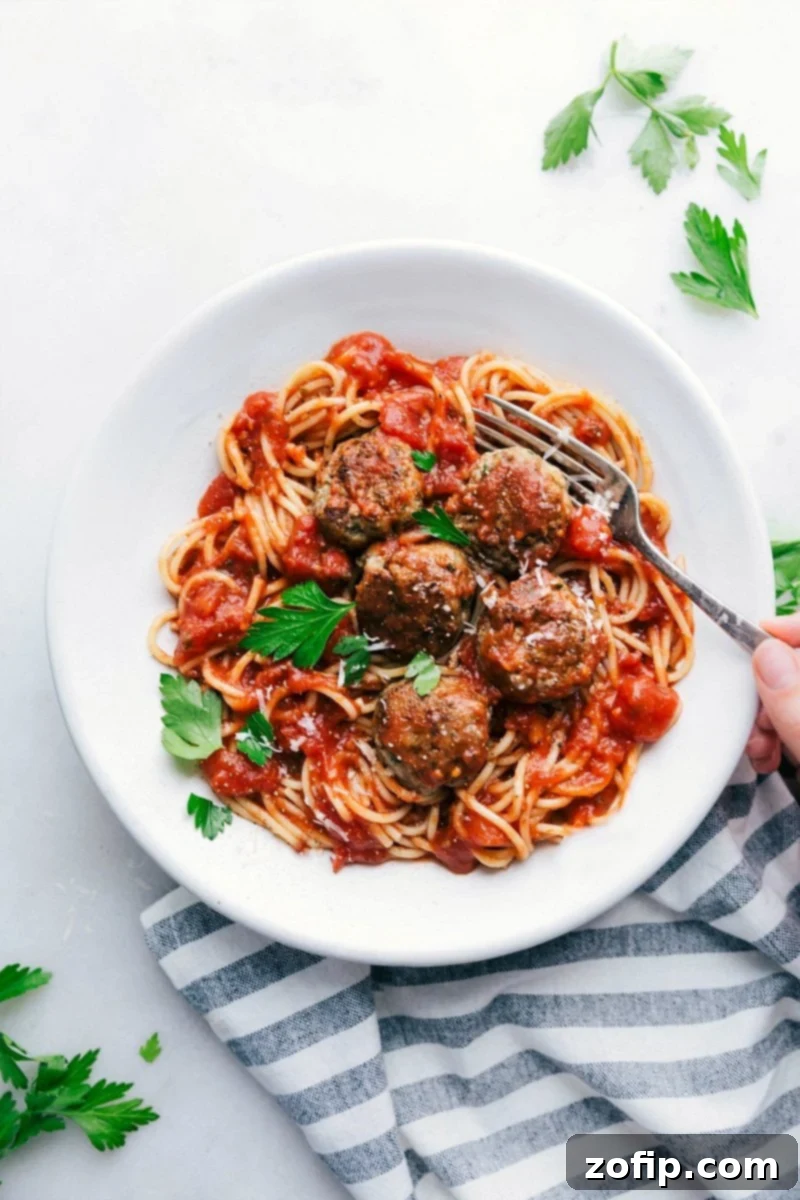A bowl of finished turkey meatballs nestled over a bed of spaghetti, generously coated with marinara sauce and topped with fresh herbs, creating a hearty and inviting meal ready to be enjoyed.