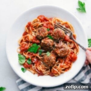 A bowl of finished turkey meatballs nestled over a bed of spaghetti, generously coated with marinara sauce and topped with fresh herbs, creating a hearty and inviting meal ready to be enjoyed.