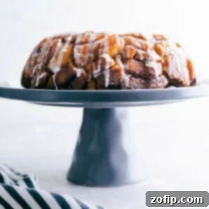 Cinnamon roll monkey bread baked and ready to eat, sitting on a cake stand, with icing dripping, delicious and full of flavor.