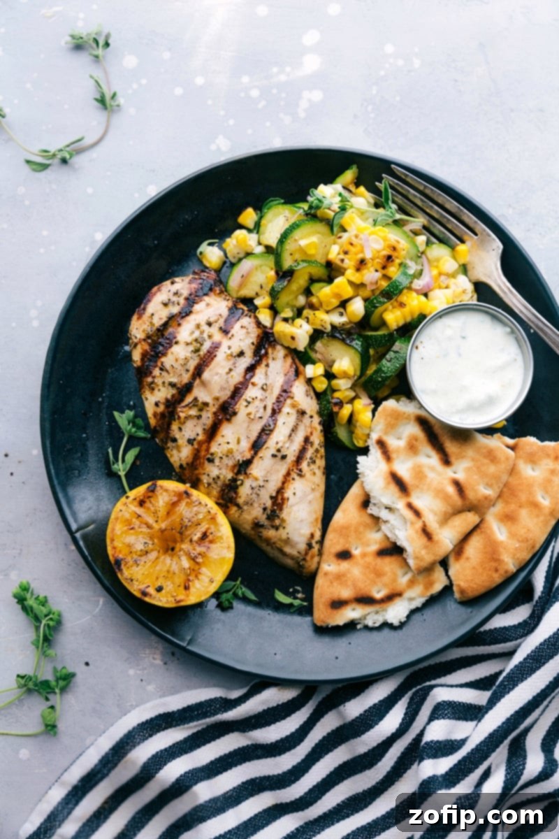 A plate featuring Greek chicken served with naan bread and a zucchini and corn salad, offering a delicious and flavor-packed meal.