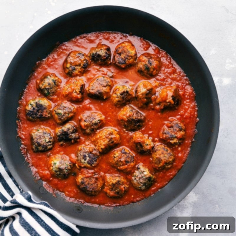 Tender, browned meatballs gently simmering in a rich, homemade marinara sauce within a large pan, infusing every bite with deep, savory flavors for the meatball sub recipe.