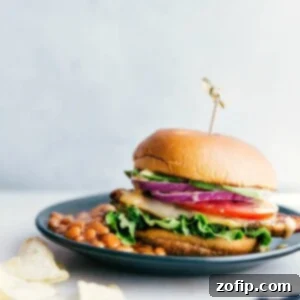 A chicken burger on a plate accompanied by a side of baked beans, presenting a delicious and satisfying meal, ready for enjoyment.