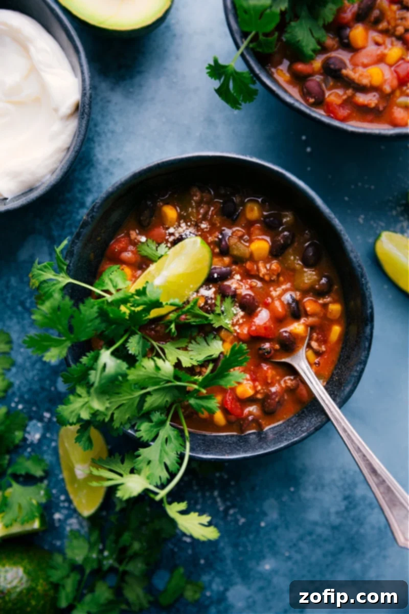 Overhead image of a bowl of rich Taco Chili topped with cheese, sour cream, and cilantro.