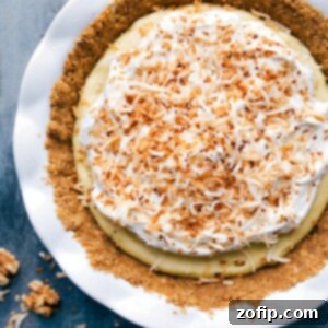 A delectable slice of homemade Coconut Cream Pie on a white plate, showcasing the creamy filling, graham cracker crust, and fluffy whipped cream topping adorned with toasted coconut flakes.