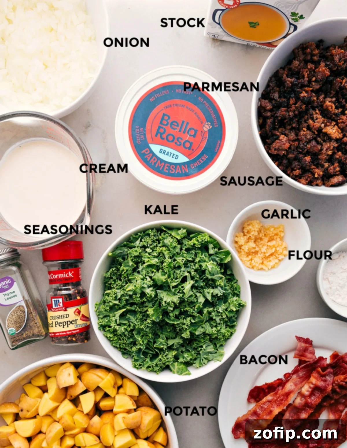 All the fresh ingredients for Zuppa Toscana soup laid out and prepped: chicken stock, onion, Parmesan, sausage, cream, kale, garlic, flour, seasonings, bacon, and potatoes.