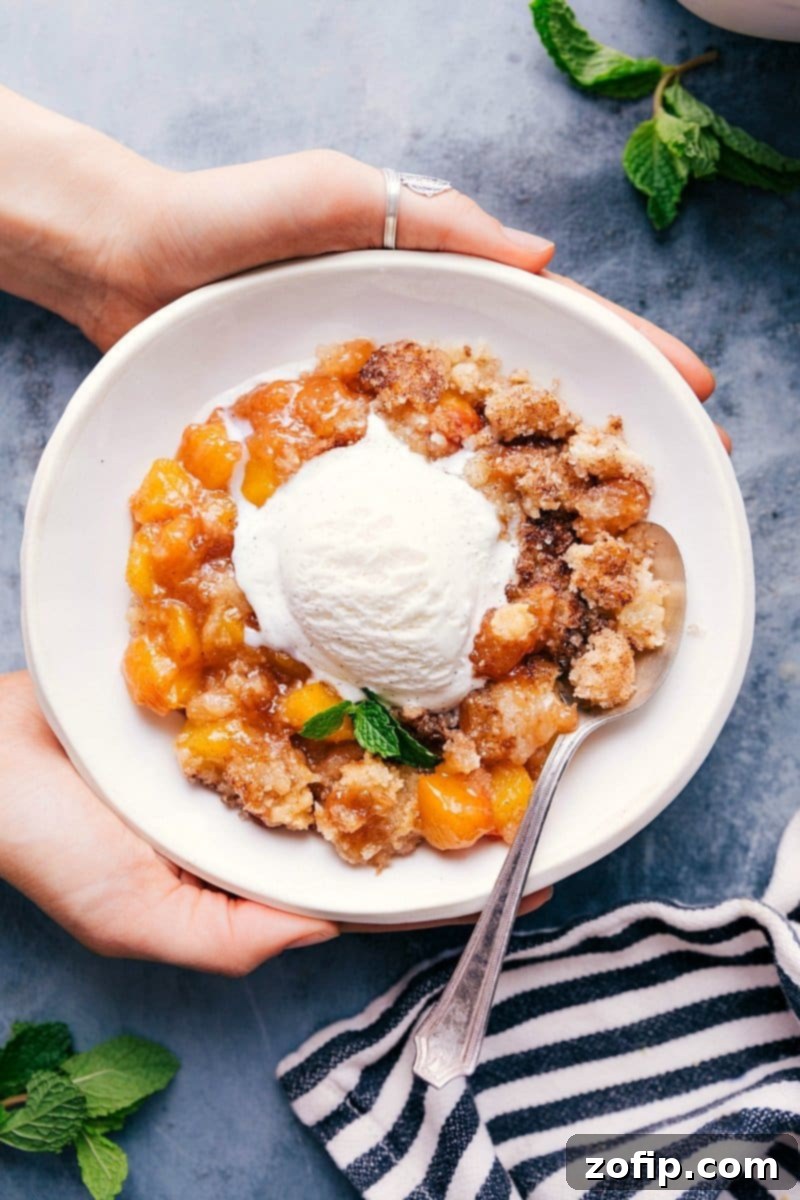 Sweet and delicious peach cobbler in a bowl with a scoop of vanilla ice cream on top, ready to be enjoyed.