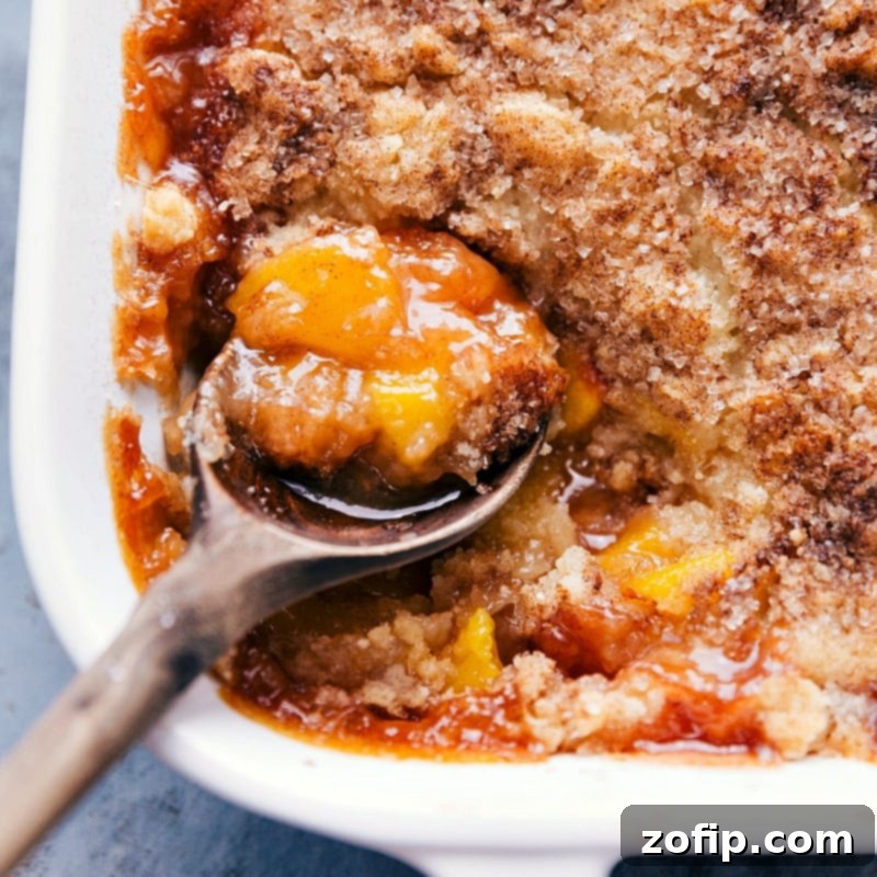 A spoonful of the dessert being scooped out of the casserole dish, revealing the delicious fruity interior and golden topping.