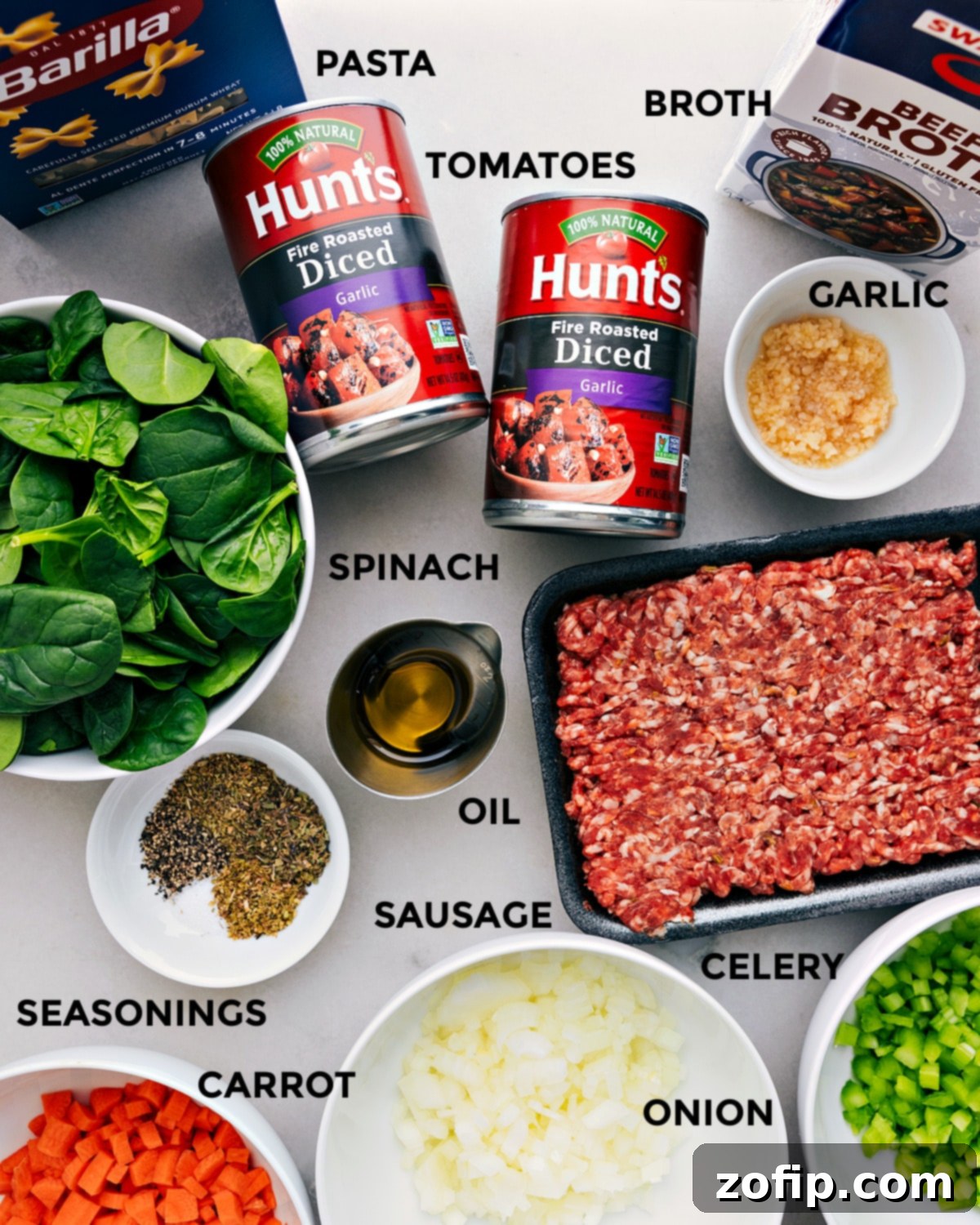 All the essential ingredients for a delicious pasta soup laid out: robust beef broth, aromatic garlic, sweet diced tomatoes, various pasta shapes, savory Italian sausage, fresh spinach, olive oil, and a selection of seasonings and mirepoix vegetables.