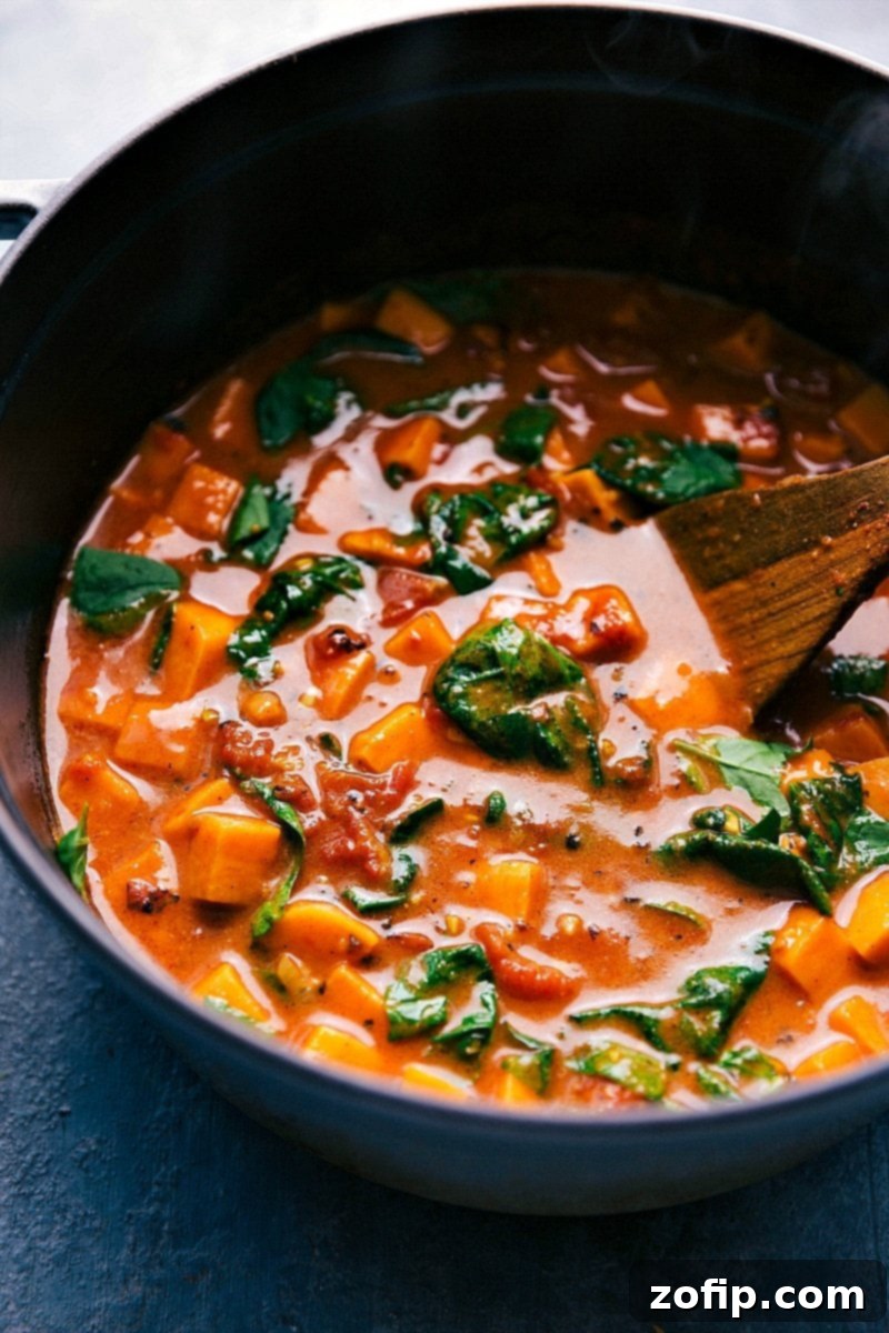 A large pot filled with rich, warm, and aromatic sweet potato curry, ready to be served, with a spoon resting in the pan, showcasing its creamy texture and vibrant colors.
