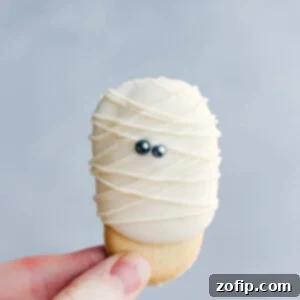 Bandaged Cookie Delights 2 An adorable and festive mummy cookie being held, decorated with white icing and eyes to resemble a mummy, perfect for Halloween.