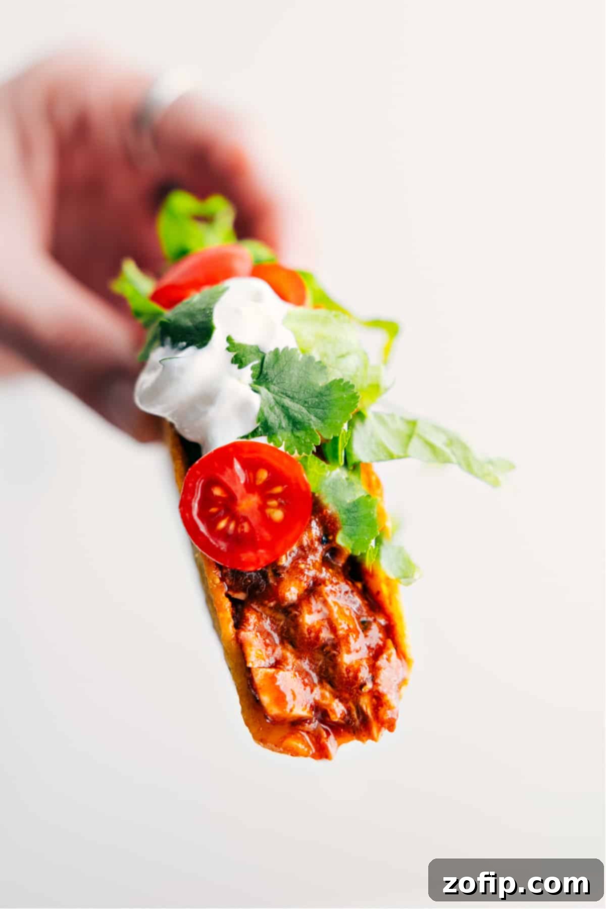 Quick 30-Minute Dinner: Rotisserie Chicken Tacos A hand holding a beautifully assembled rotisserie chicken taco, generously topped with cool sour cream, diced red tomatoes, and fresh green cilantro, showcasing a perfect quick and satisfying dinner.