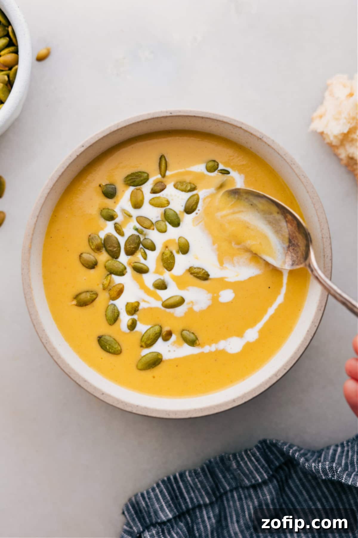 A steaming bowl of vibrant orange butternut squash soup, garnished with crunchy pepitas.