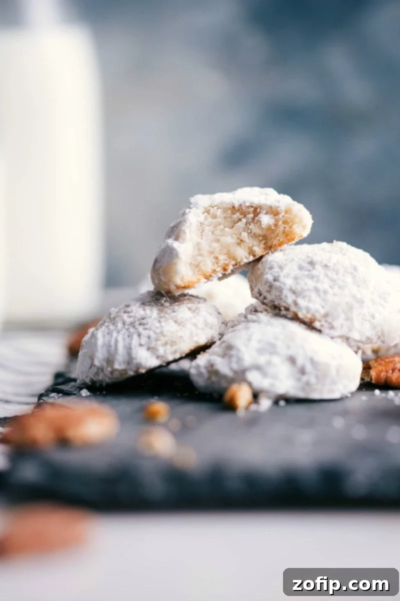 Stack of Mexican Wedding Cookies with a bite taken out of one, revealing the fluffy interior and pecan pieces.